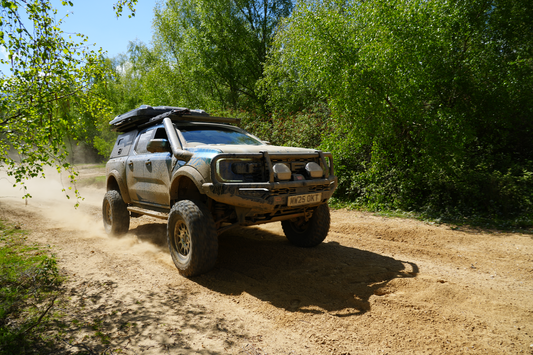 Modified Ford Ranger Raptor driving a dusty trail with roof tent, snorkel and bull bar