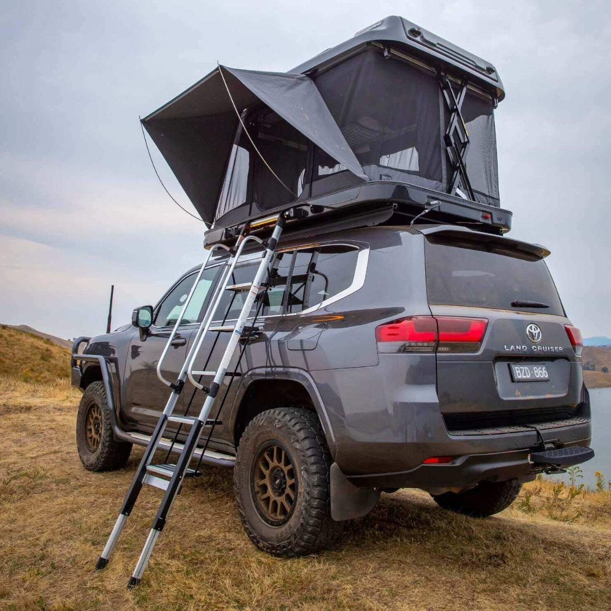 Gray Toyota Land Cruiser with a rooftop tent and ladder in a natural setting.