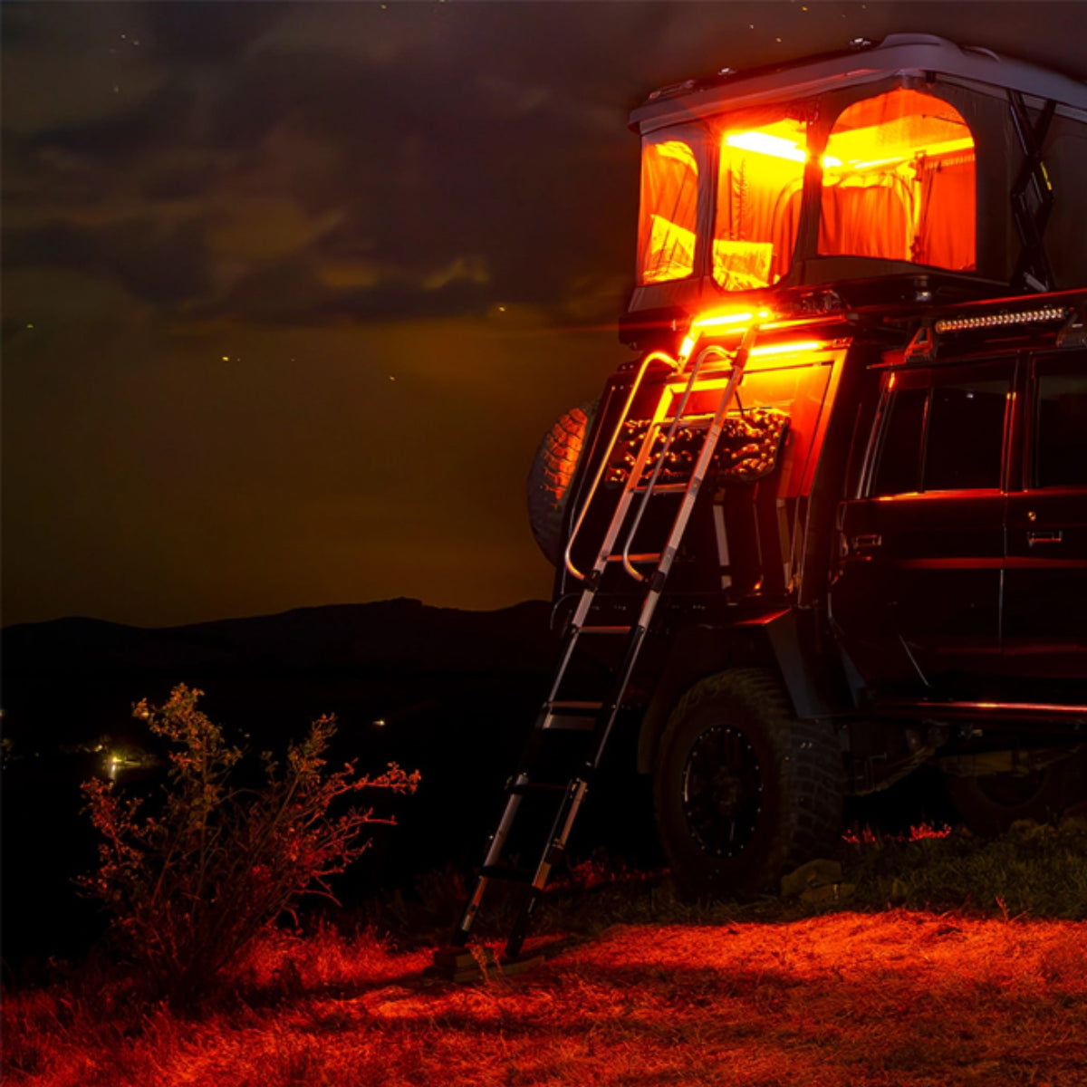 Off-road vehicle with open roof and ladder at night in a desert landscape