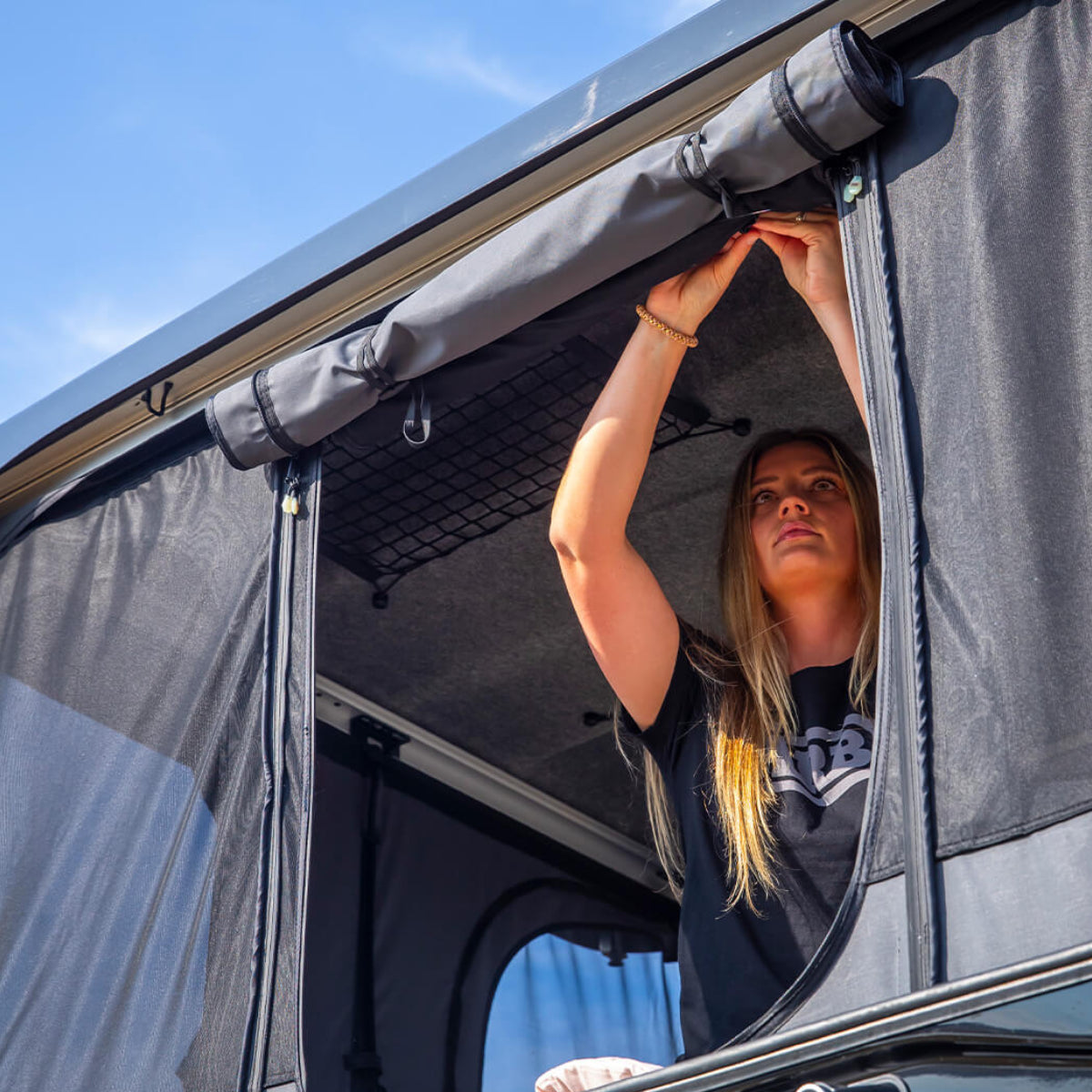 Person looking out of a vehicle with an open roof tent on a sunny day.