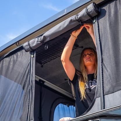 Person looking out of a vehicle with an open roof tent on a sunny day.