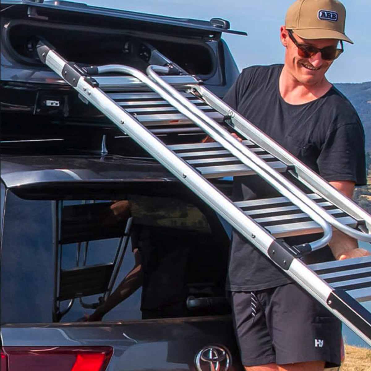 Man removing ladder form roof tent on a car with a clear sky background