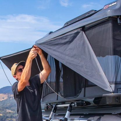 Person adjusting a roof top tent on a vehicle with a scenic background