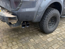 Gray truck with off-road tires on a paved surface and side twin tip exhaust.