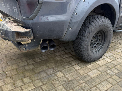 Gray truck with off-road tires on a paved surface and side twin tip exhaust.