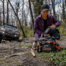 Packing the ARB Premium Recovery Kit bag beside a 4x4 on a muddy trail